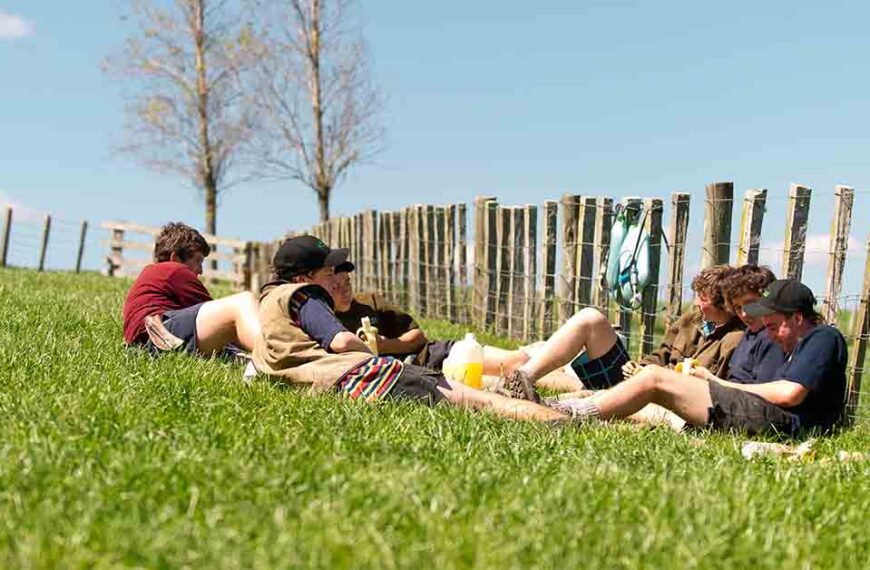 Young farm workers sit against a fence in a paddock.